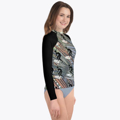 Child in a long-sleeved Surfer's Paradise rash guard featuring a fun cartoon graphic