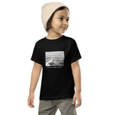 Child wearing a black surf graphic t-shirt with words "Right at Your Heels" underneath the graphic.