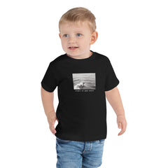 Toddler wearing a black surf graphic tee with sentence "Right at Your Heels" under graphic.