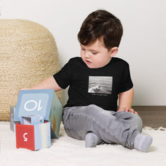 Toddler playing with toys wearing a black surf t-shirt with sentence "Right at Your Heels" underneath the graphic.